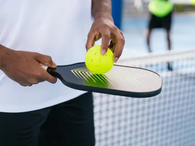 Hand holding pickleball paddle and ball