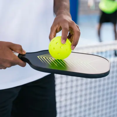 Hand holding pickleball paddle and ball